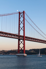 Sailing boat in the Tagus River passing by the 25 of April Bridge (Ponte 25 de Abril), in the city of Lisbon, Portugal; Concept for travel in Portugal