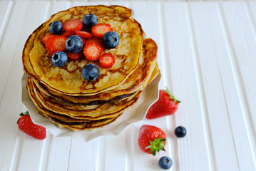 A stack of pancakes decorated with berries. delicious pancakes, with fresh blueberries, strawberries and maple syrup on a light background. With copy space. Top view.