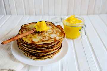 A stack of homemade pancakes on a white plate on a light wooden table. Pancakes are served with GHEE oil. This oil is very healthy. Copy space. Rustic.