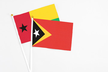 East Timor and Guinea Bissau stick flags on white background. High quality fabric, miniature national flag. Peaceful global concept.White floor for copy space.