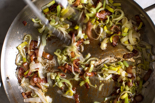 Close up of sauteed leeks, garlic and bacon on frying pan