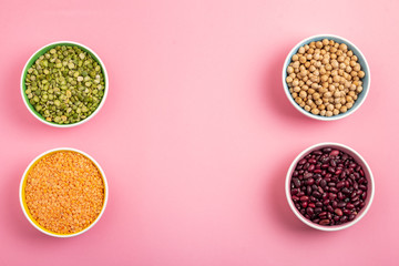 Dried beans, lentils, green horn and chickpeas in round plates on a pink background