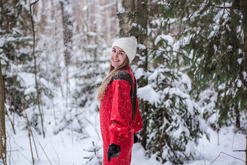 Young happy woman wearing a red dress and play with snow in the forest. Happy winter time. Christmas time concept. Snowy forest in winter. Belarus, Minsk.