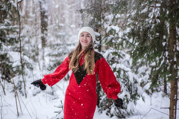 Young happy woman wearing a red dress and play with snow in the forest. Happy winter time. Christmas time concept. Snowy forest in winter. Belarus, Minsk.