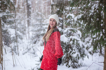 Fototapeta na wymiar Young happy woman wearing a red dress and play with snow in the forest. Happy winter time. Christmas time concept. Snowy forest in winter. Belarus, Minsk.
