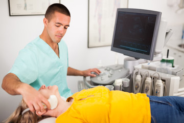Man doctor conducting ultrasound examination of patient's thyroid lying