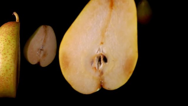 Pieces of pear cut in half fly and rotate on a black background