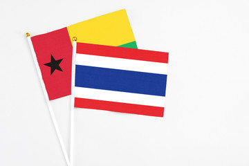 Thailand and Guinea Bissau stick flags on white background. High quality fabric, miniature national flag. Peaceful global concept.White floor for copy space.