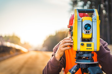 Surveyor engineer with equipment (theodolite or total positioning station) on the construction site of the road or building with construction machinery background - obrazy, fototapety, plakaty
