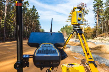 Surveyors equipment (theodolite or total positioning station) on the construction site of the road or building with construction machinery background - obrazy, fototapety, plakaty