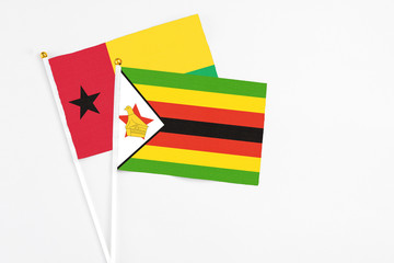 Zimbabwe and Guinea Bissau stick flags on white background. High quality fabric, miniature national flag. Peaceful global concept.White floor for copy space.