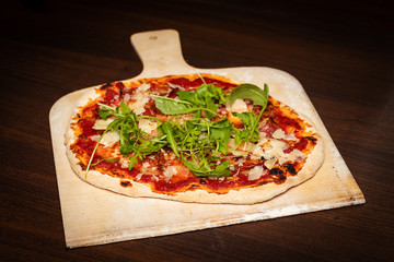 Handgemachte Pizza mit Parmesan und Ruccola, auf Holzschieber, frisch aus dem Ofen
