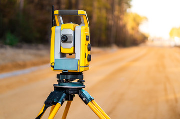 Fototapeta premium Surveyors equipment (theodolite or total positioning station) on the construction site of the road or building with construction machinery background