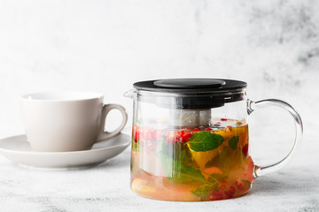 Glass teapot of cranberry, orange and mint or yellow tea with white cup isolated on bright marble background. Overhead view, copy space. Advertising for cafe menu. Coffee shop menu. Horizontal photo.