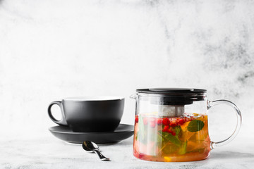 Glass teapot of cranberry, orange and mint or yellow tea on black cup isolated on bright marble background. Overhead view, copy space. Advertising for cafe menu. Coffee shop menu. Horizontal photo.