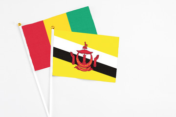 Brunei and Guinea stick flags on white background. High quality fabric, miniature national flag. Peaceful global concept.White floor for copy space.