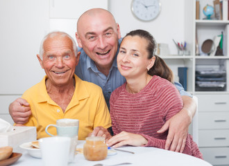 Fototapeta na wymiar Mature man with daughter and her husband at table with cup of tea