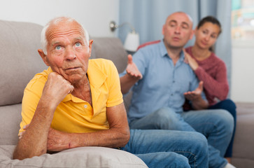 Upset senior man  sitting at home on comfortable sofa, adult children