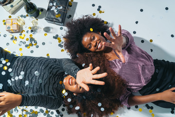 Top view of Two Happy American African Women laying on the floor celebrating new years eve with confetti, gifts and champagne.