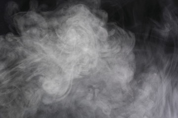 Puffs of white, gray smoke spread on a black background, curling in a fancy dance.