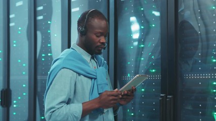 Handsome african IT specialist working in data center setting server hardware in rack cabinets. Smart black technician in computer security complex.
