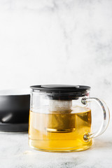 Glass teapot with dark cup of green, camomile, chamomile or yellow tea isolated on bright marble background. Overhead view, copy space. Advertising for cafe menu. Coffee shop menu. Vertical photo.