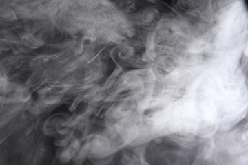 Obraz premium Puffs of white, gray smoke spread on a black background, curling in a fancy dance.