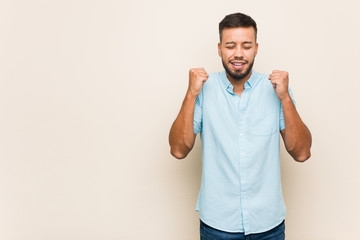 Fototapeta premium Young south-asian man raising fist, feeling happy and successful. Victory concept.