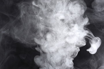 Puffs of white, gray smoke spread on a black background, curling in a fancy dance.