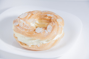 Obraz na płótnie Canvas Ring donut cut in the middle and inside whipped cream and on the top almond slices and sugar powder on white plate on bright background with space for text.