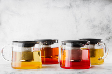 Glass teapots with four kinds of tea. Black tea, green tea isolated on bright marble background. Overhead view, copy space. Advertising for cafe menu. Coffee shop menu. Horizontal photo.