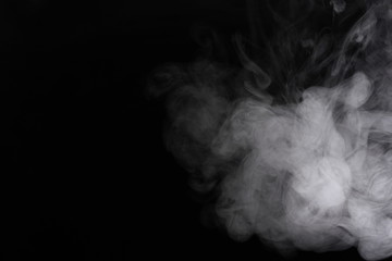 Puffs of white, gray smoke spread on a black background, curling in a fancy dance.