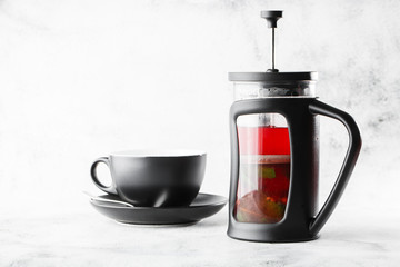 Cranberry, red or raspberry tea in french press with dark cup isolated on bright marble background....