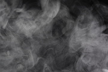 Puffs of white, gray smoke spread on a black background, curling in a fancy dance.