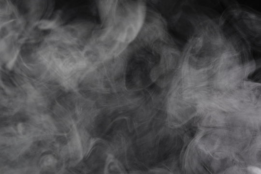 Puffs of white, gray smoke spread on a black background, curling in a fancy dance.