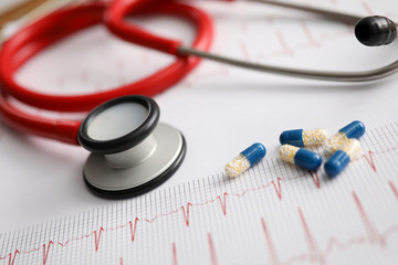 Red stethoscope with pill lie on table against