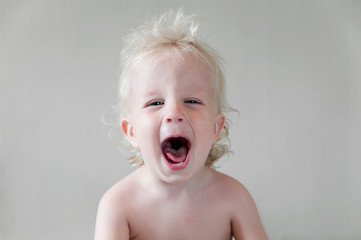 blue-eyed blond kid laughing with his mouth wide open on a gray background