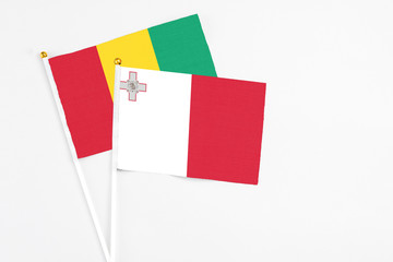 Malta and Guinea stick flags on white background. High quality fabric, miniature national flag. Peaceful global concept.White floor for copy space.