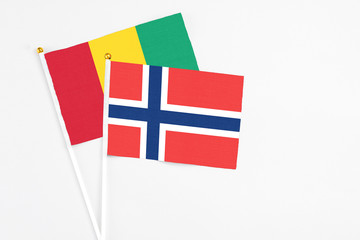 Norway and Guinea stick flags on white background. High quality fabric, miniature national flag. Peaceful global concept.White floor for copy space.