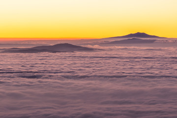 Distant mountains above a sea of fog like islands at sunset