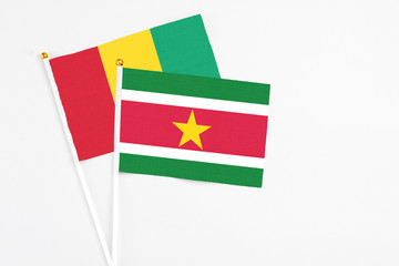 Suriname and Guinea stick flags on white background. High quality fabric, miniature national flag. Peaceful global concept.White floor for copy space.