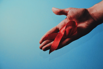 Aids red ribbon on man's hand support for World aids day and national HIV AIDS and aging awareness month concept. Blue background