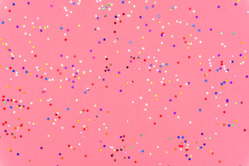 Photo of multi-colored stars glitter sprinkles on pink trendy background. Festive holiday background for your projects. Celebration concept. Christmas pattern. Top view, flat lay