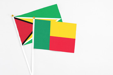 Benin and Guyana stick flags on white background. High quality fabric, miniature national flag. Peaceful global concept.White floor for copy space.