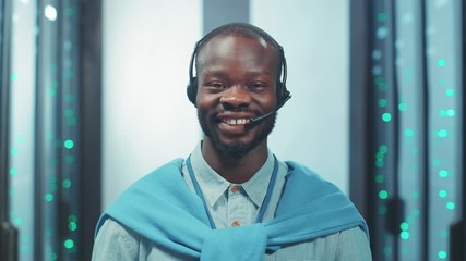 Cheerful african american server engineer standing in digital corridor of server room. Indoor portrait ambitious black specialist working at network and data center. - Powered by Adobe