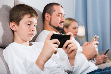 Parents with son using mobile gadgets at home