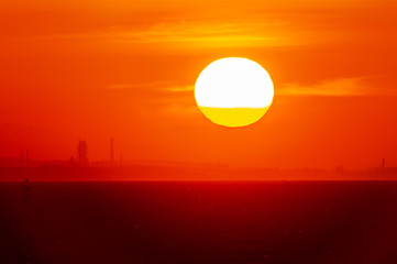 海と工場シルエットを染めて昇る朝日