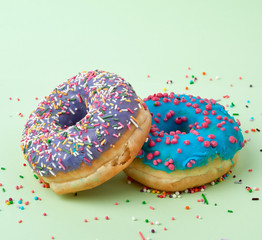round baked donut with colored sugar sprinkles and with blue sugar icing on a green background