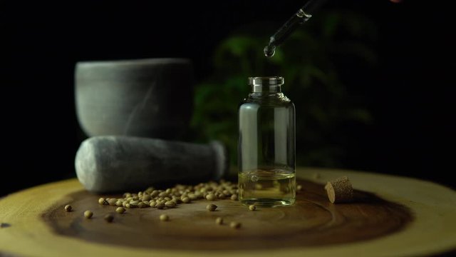 Macro close up of droplet pipette dosing biological and ecological oil of the hemp plant.  Pharmaceutical herbal cbd oil in the small jar on the wood circle tree ring table. Organic pharma concept.