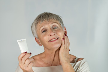 beautiful older woman with White  and gray hair with blue eyes smiling and with bottle of cosmetic...